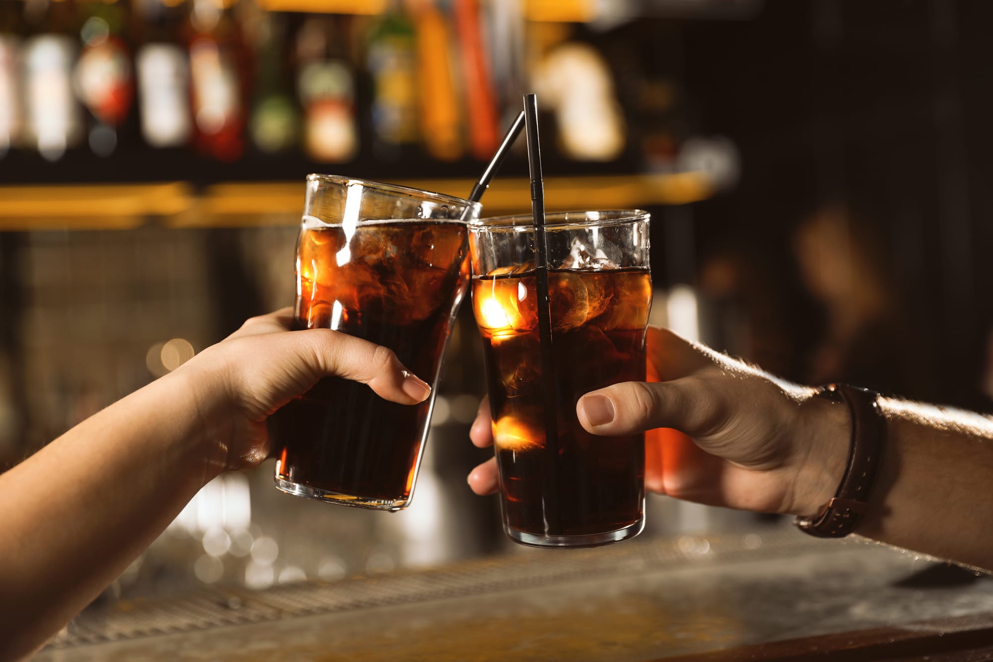 Two people touching glasses filled with cola
