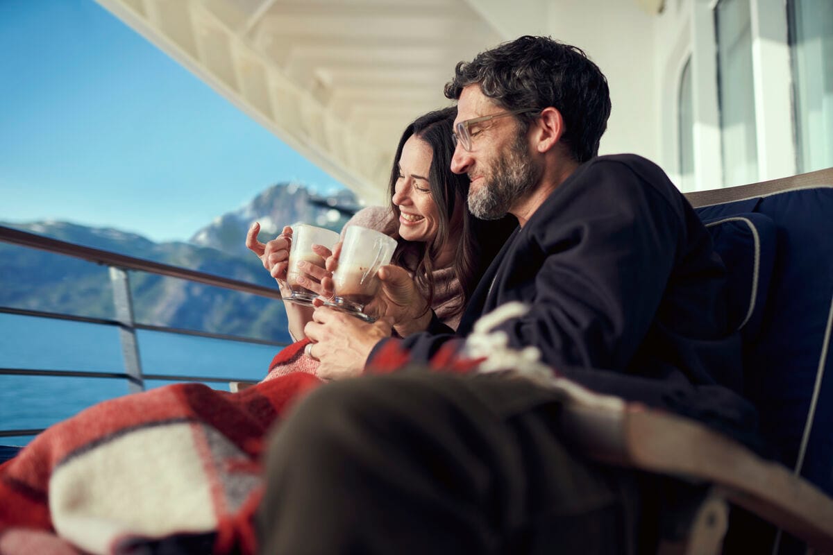 A couple drinking hot chocolate while sitting under blankets outside on a cruise ship