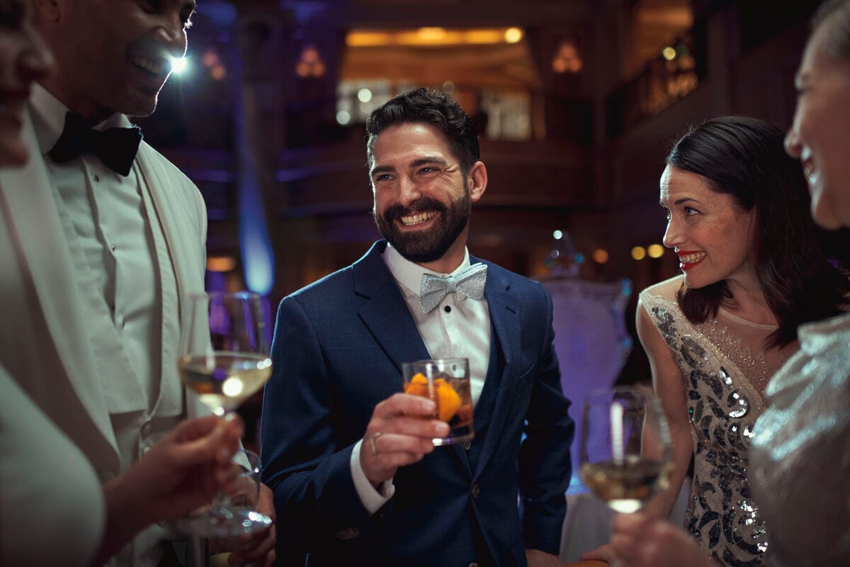 A group standing and enjoying drinks, dressed in formal wear