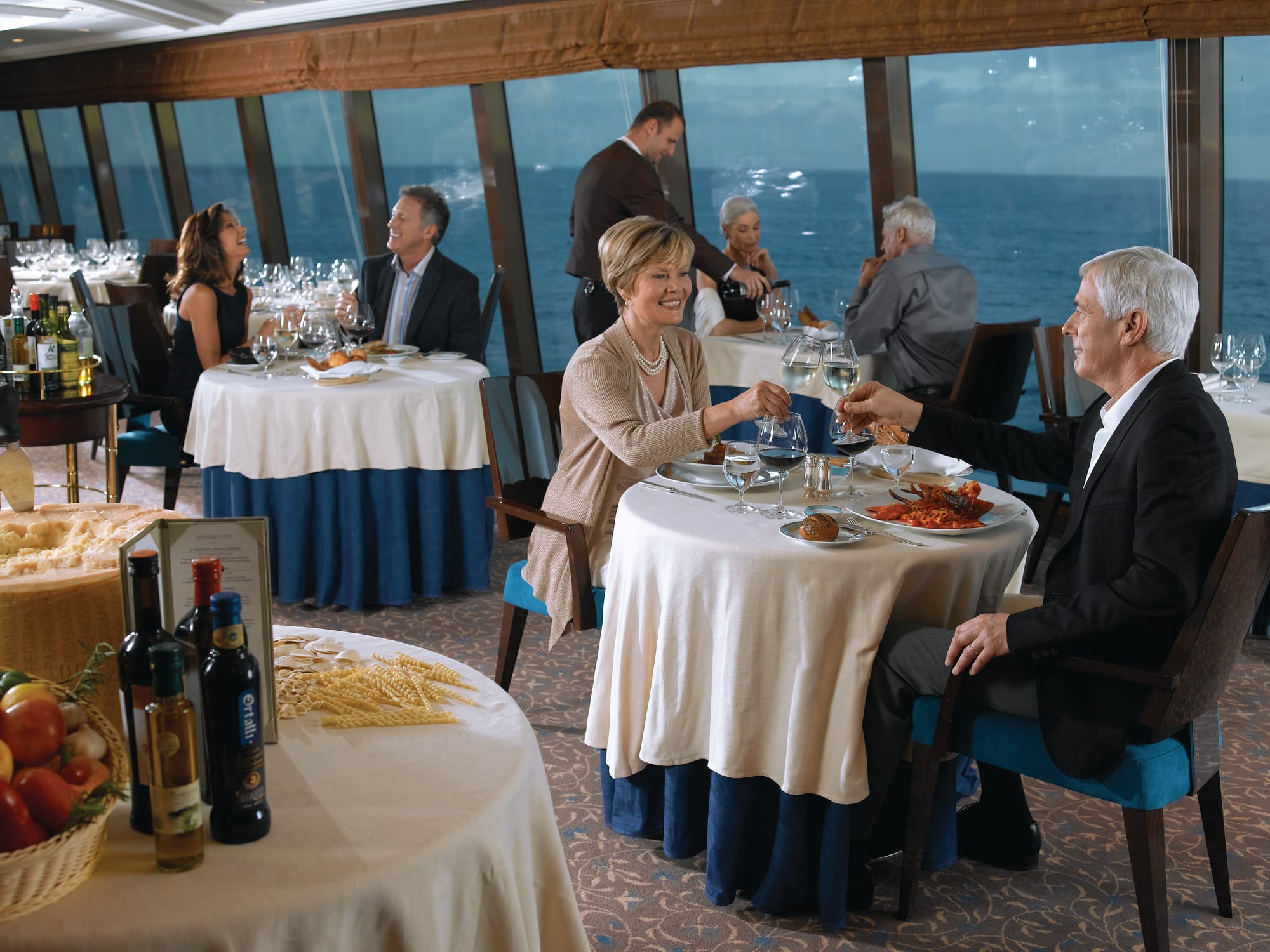 An image of a couple dining at a restaurant on a cruise ship, with panoramic ocean views in the background