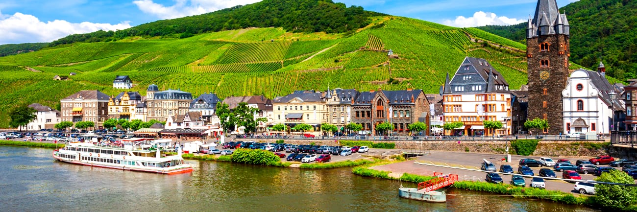 A river cruise ship passing by a small riverside village with rolling green hills in the background